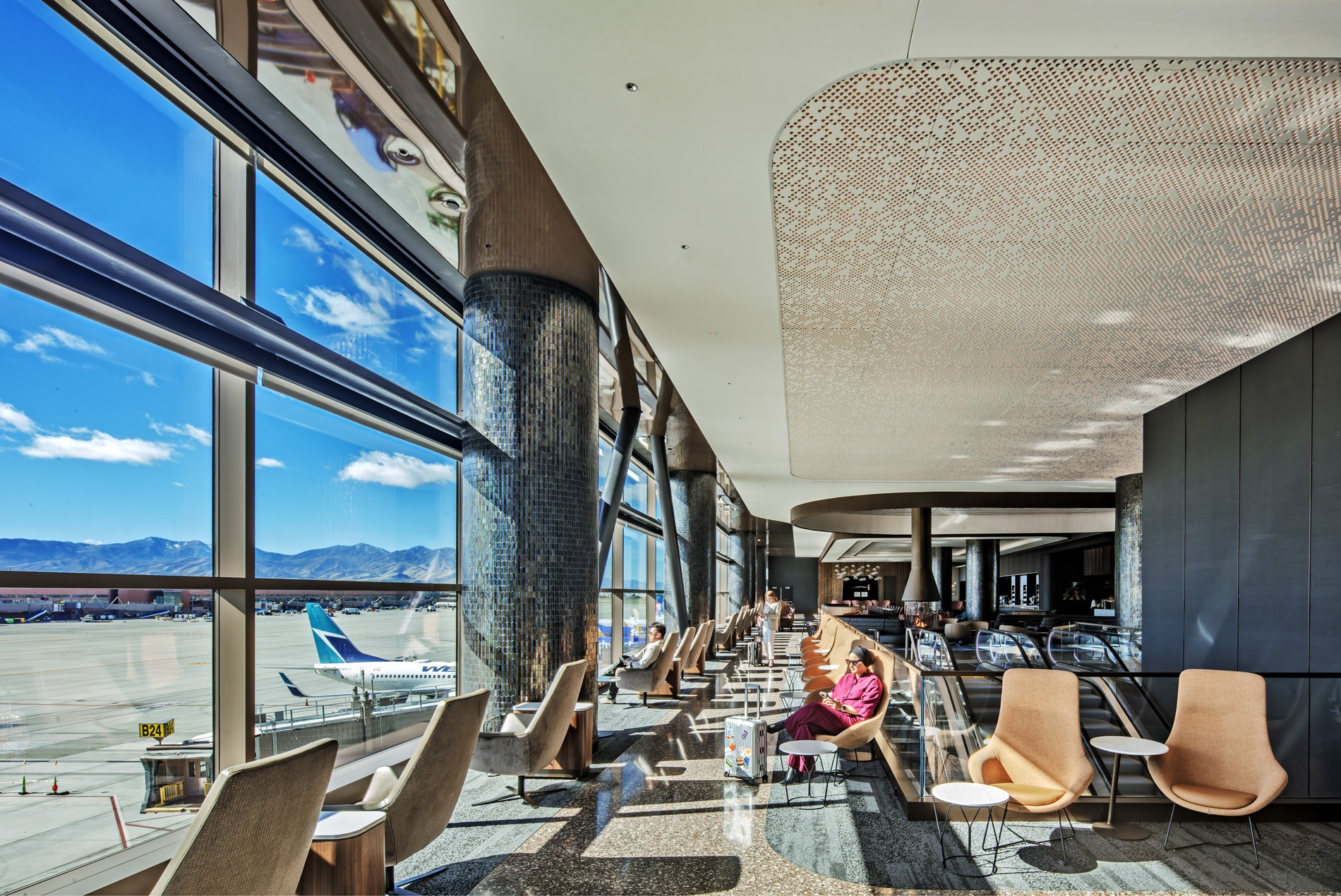 Traveler sitting in comfortable lounge seating with floor-to-ceiling views of the airfield and Wasatch Mountains at the HOK-designed Delta Sky Club at Salt Lake City International Airport